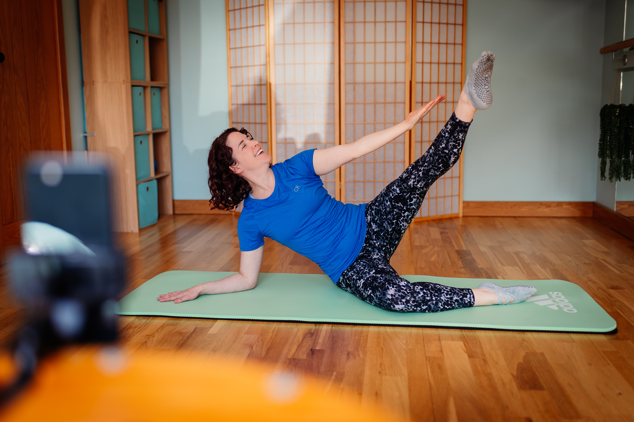 Emmeline Kemp, owner of Green Room Health, demonstrating a stretch on the mat for online members who enjoy home Pilates and Barre workouts.