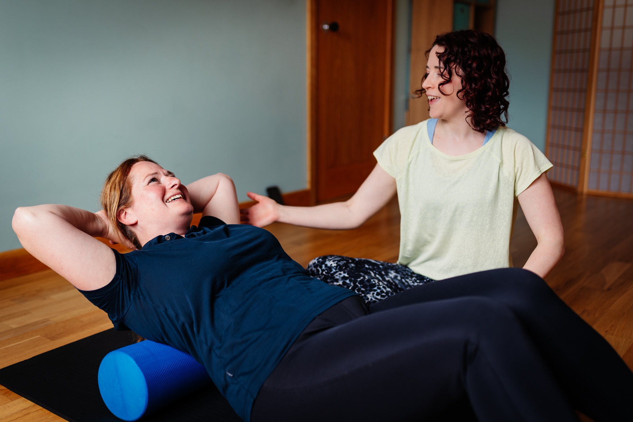 Emmeline Kemp, owner of Green Room Health, teaching a client Pilates ab curls on the mat using a blue foam roller. 